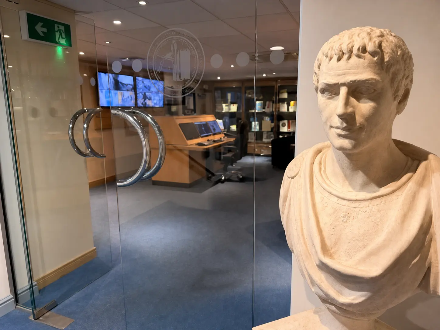 Centurion monitoring showroom viewed through glass beside a Caesar bust